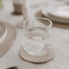 Glas mit Wasser und Muschelmotiv am Boden auf Untersetzer im natürlichen Wohnambiente