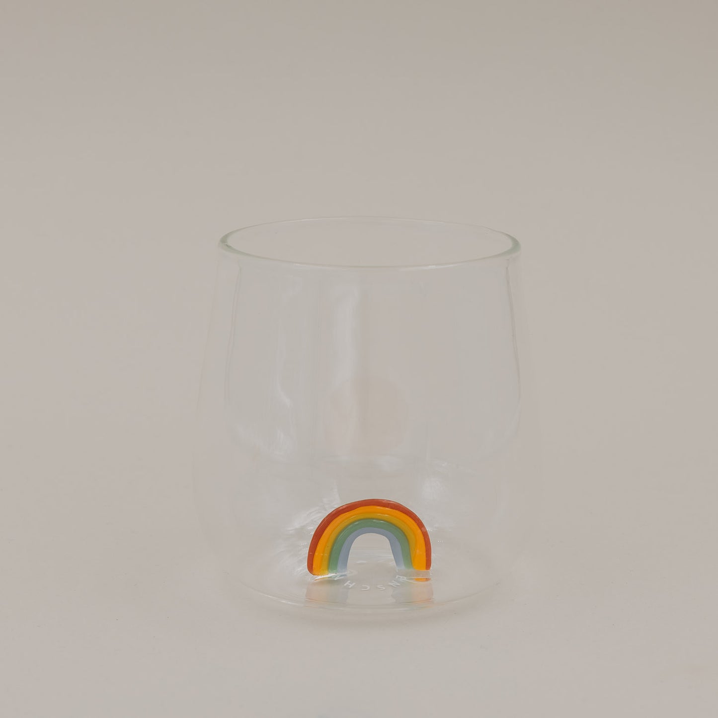 Klares Trinkglas mit buntem Regenbogen am Boden, schlichtes Design freigestellt