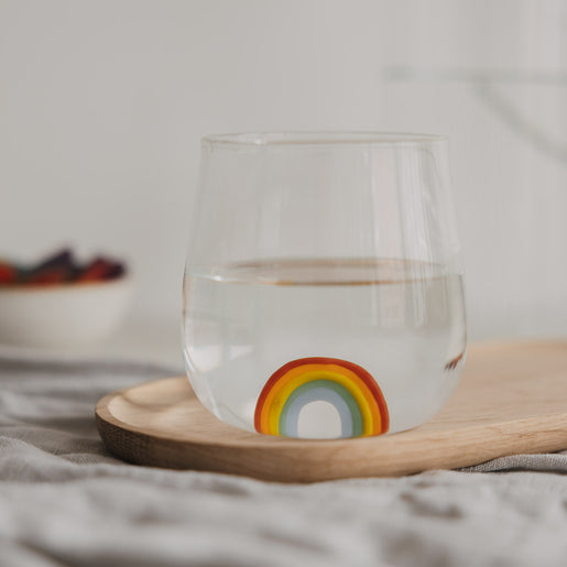Trinkglas mit Regenbogen Motiv gefüllt mit Wasser, dekorativ auf Holzbrett arrangiert