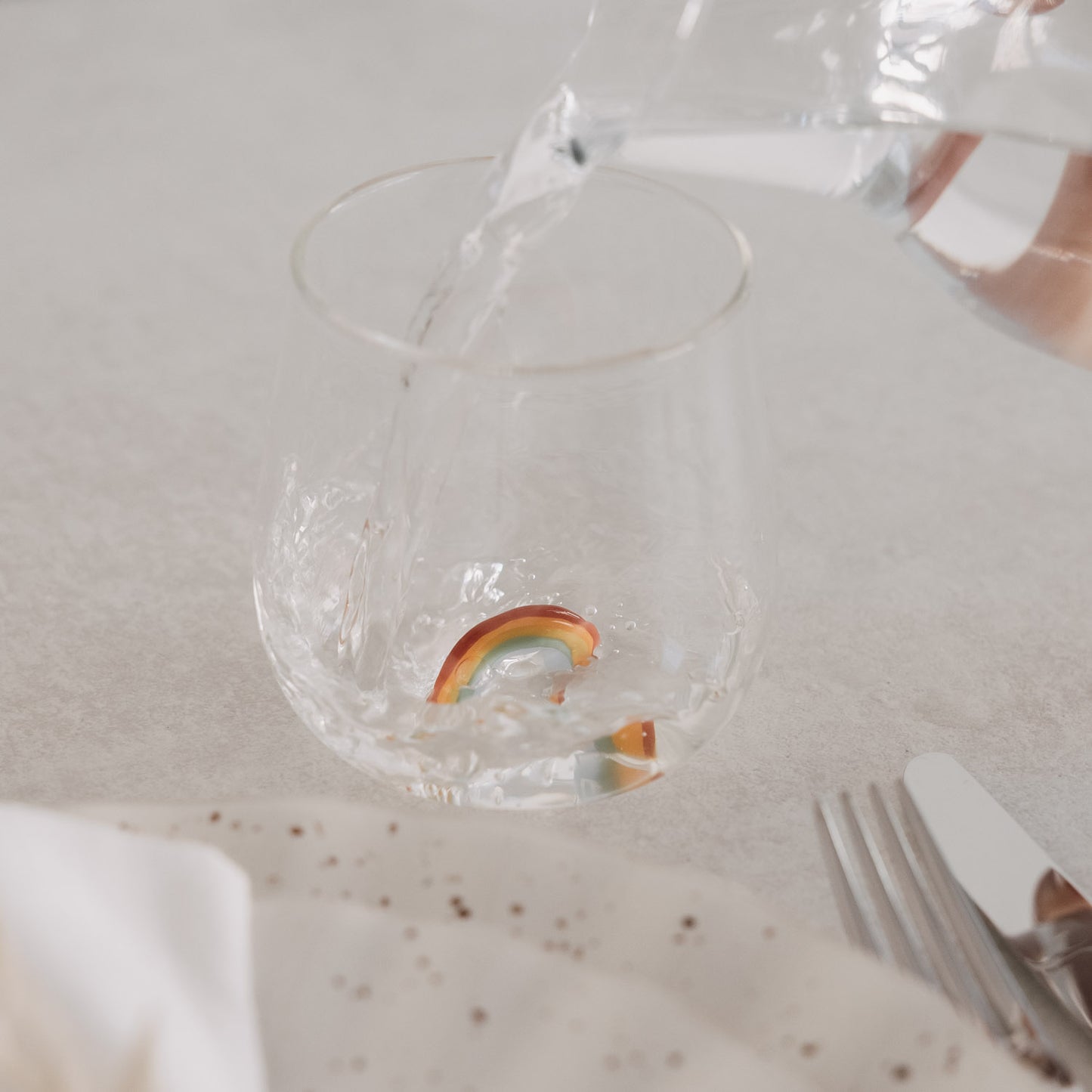 Transparentes Glas mit Regenbogen-Design wird mit Wasser befüllt, modernes Doppelwandglas auf gedecktem Tisch