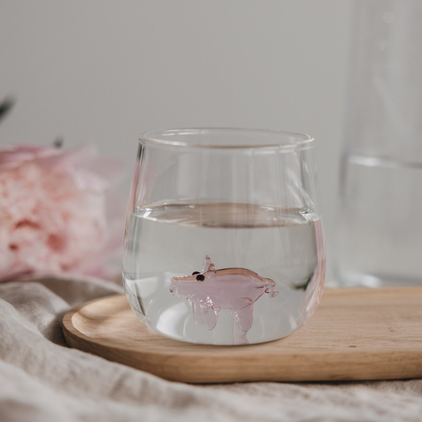 Trinkglas mit Schwein Motiv gefüllt mit Wasser auf Holzbrett, stilvolles Glas
