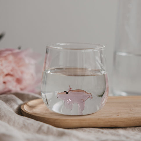 Trinkglas mit Schwein Motiv gefüllt mit Wasser auf Holzbrett, stilvolles Glas