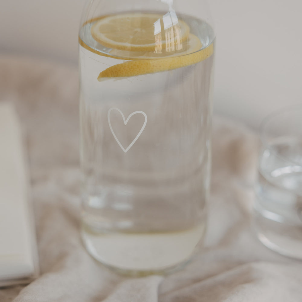 Glaskaraffe mit Wasser und Zitrone, kleines Herzmotiv, stilvolle Tischszene