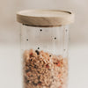 Detailaufnahme eines Vorratsglases mit schwarzen Herzen, gefüllt mit Müsli und verschlossen mit Holzdeckel.