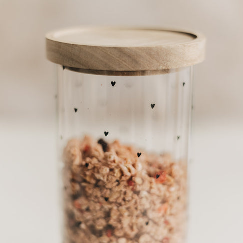 Detailaufnahme eines Vorratsglases mit schwarzen Herzen, gefüllt mit Müsli und verschlossen mit Holzdeckel.