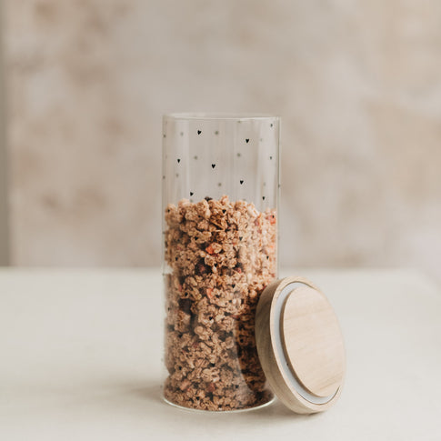 Vorratsglas mit schwarzen Herzen und Müsli, daneben der abgenommene Holzdeckel mit Dichtungsring.