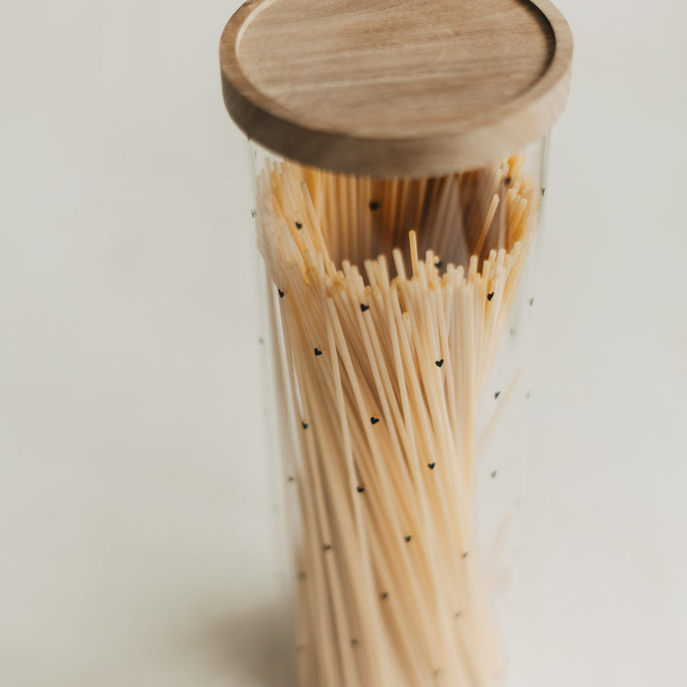 Nahaufnahme eines mit Spaghetti gefüllten Vorratsglases mit schwarzen Herzen und Holzdeckel.