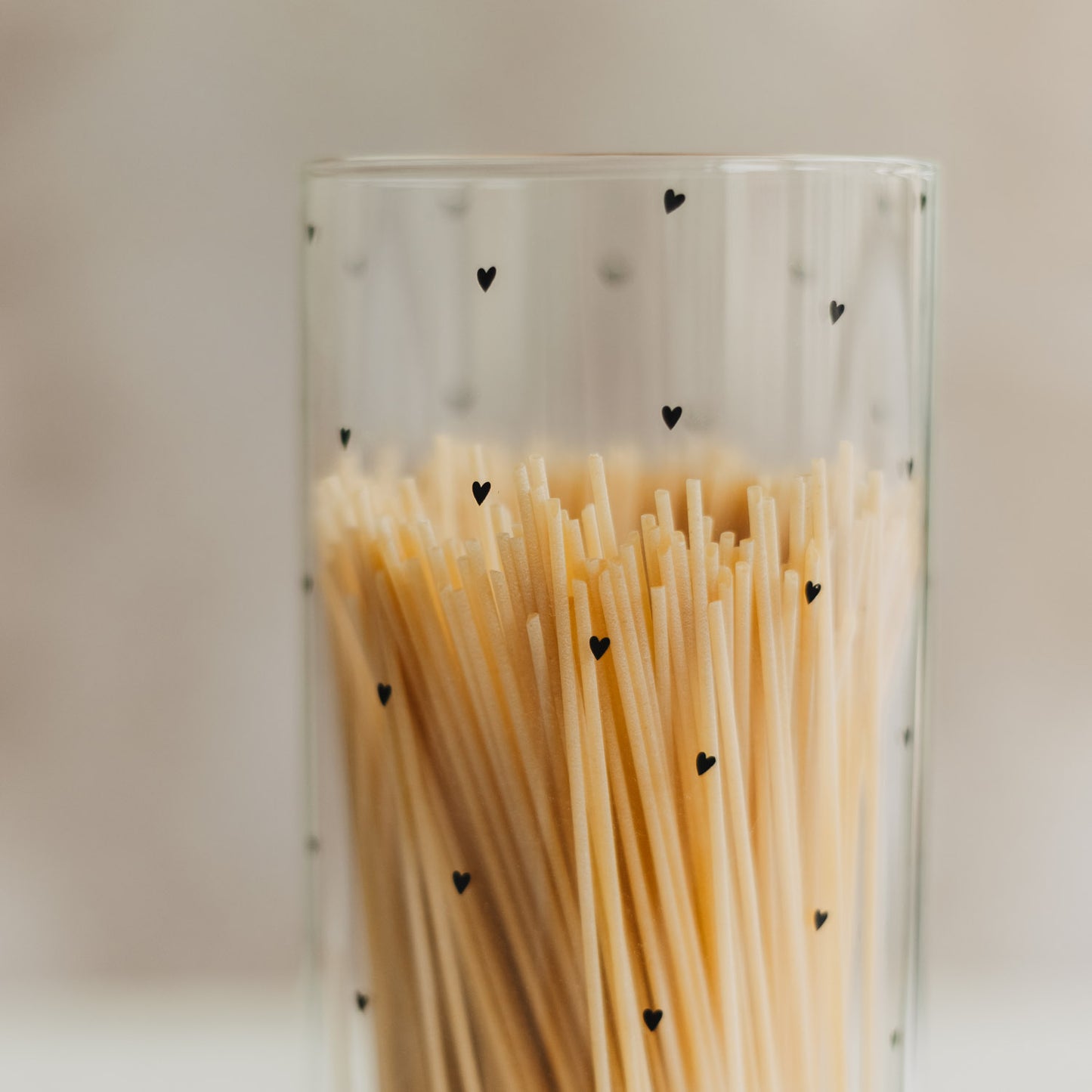 Nahaufnahme von Spaghetti in einem transparenten Vorratsglas mit kleinen schwarzen Herzen.