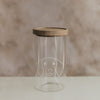 Transparentes Vorratsglas mit weißem Hundemotiv und Holzdeckel auf hellem Untergrund.