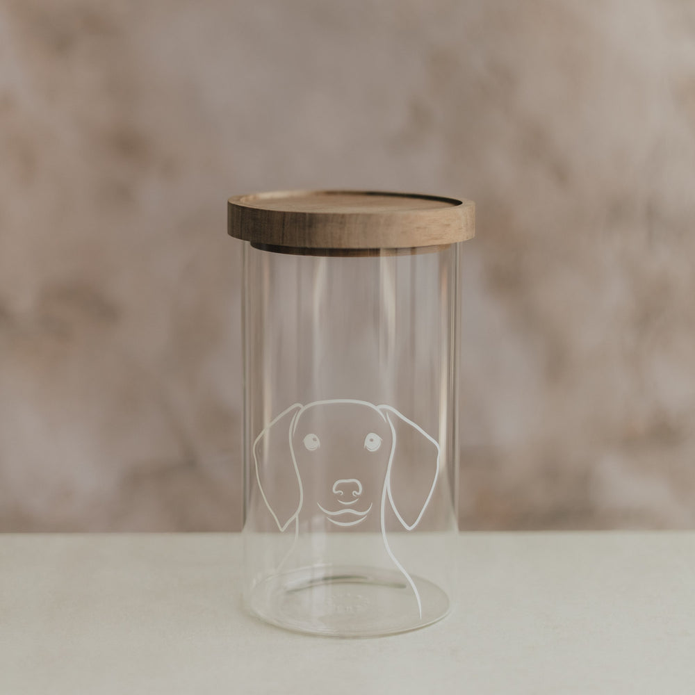 Transparentes Vorratsglas mit weißem Hundemotiv und Holzdeckel auf hellem Untergrund.