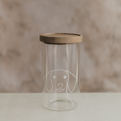 Transparentes Vorratsglas mit weißem Hundemotiv und Holzdeckel auf hellem Untergrund.