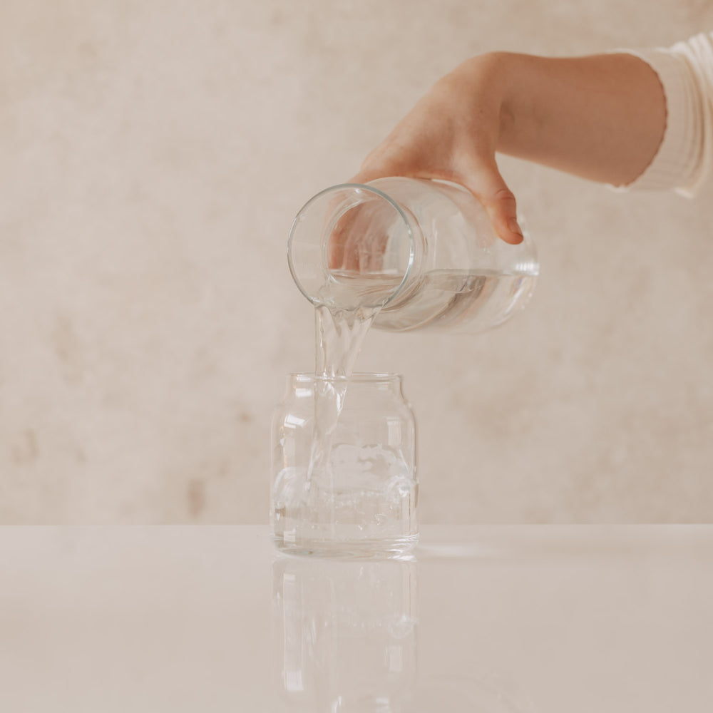 Wasser wird in Glasvase mit Herzprint gegossen, minimalistisches Setting