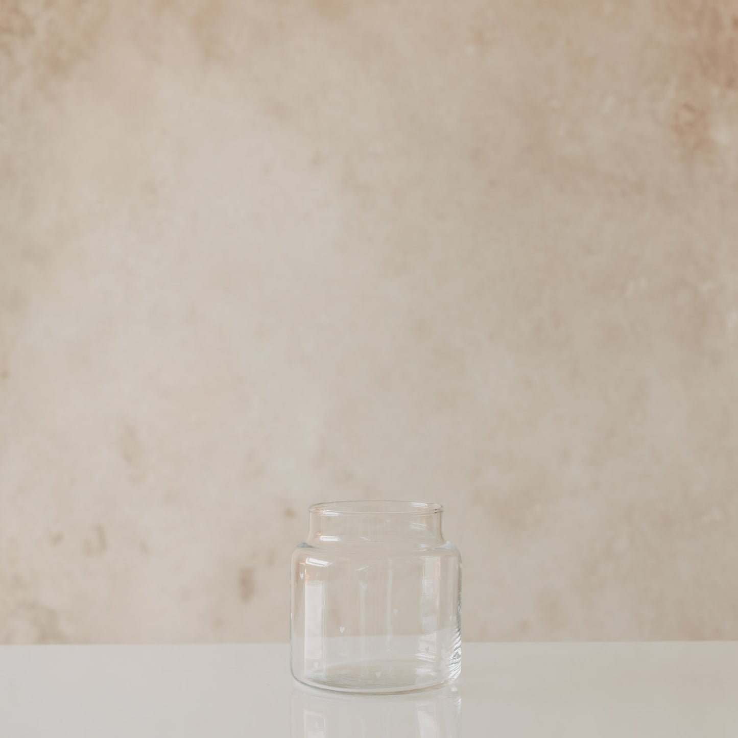 Kleine Glasvase mit Herzmuster auf hellem Tisch vor neutralem Hintergrund