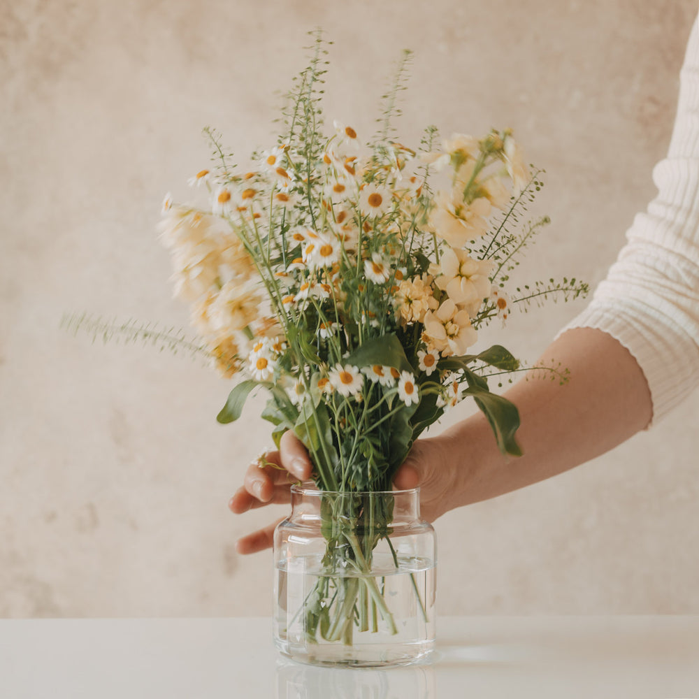 Hand arrangiert frische Blumen in Glasvase mit weißen Herzen