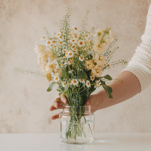 Hand arrangiert frische Blumen in Glasvase mit weißen Herzen