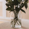 Glasvase mit weißen Herzen und Blumen auf Stoffhocker