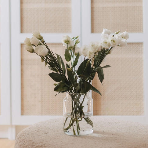 Glasvase mit weißen Herzen und Blumen auf Stoffhocker