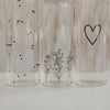 Detail Glasflaschen mit feinen Herz- und Blumenillustrationen im transparenten Design