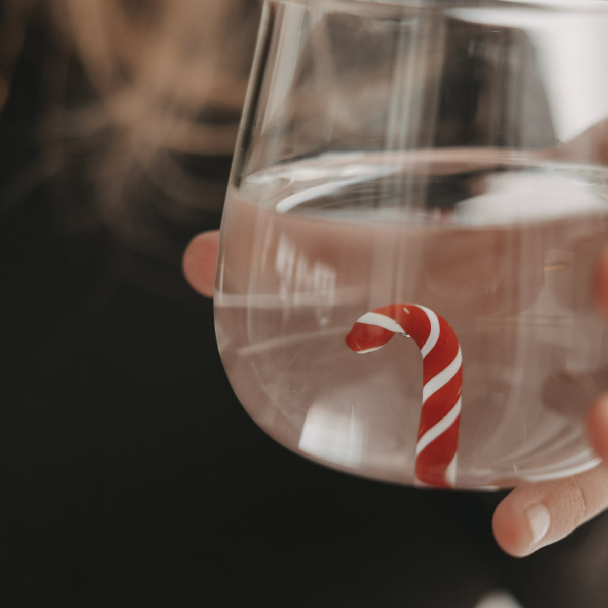 Nahaufnahme des Trinkglases mit Wasser und rot-weißer Zuckerstange als dekorative Figur im Glasboden.