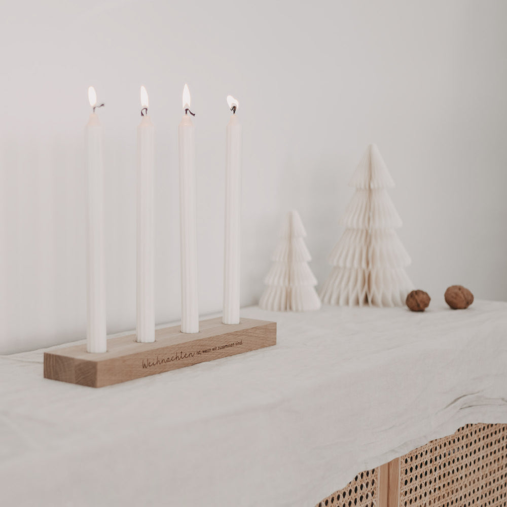 Weihnachtlicher Kerzenhalter mit vier Kerzen auf Tisch, im Hintergrund Papier-Tannenbäume