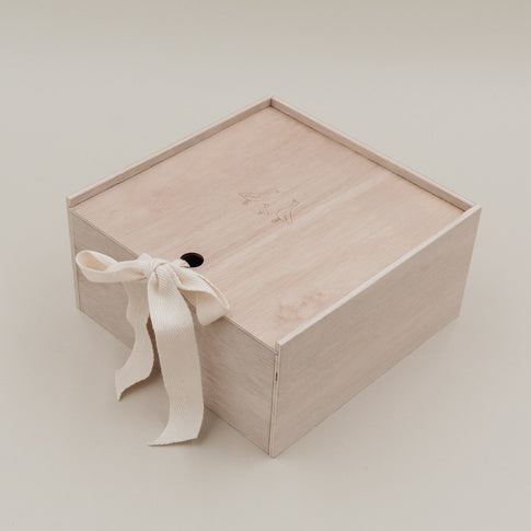 Erinnerungsbox aus hellem Holz mit Gänsegravur und Stoffschleife, frontal fotografiert.