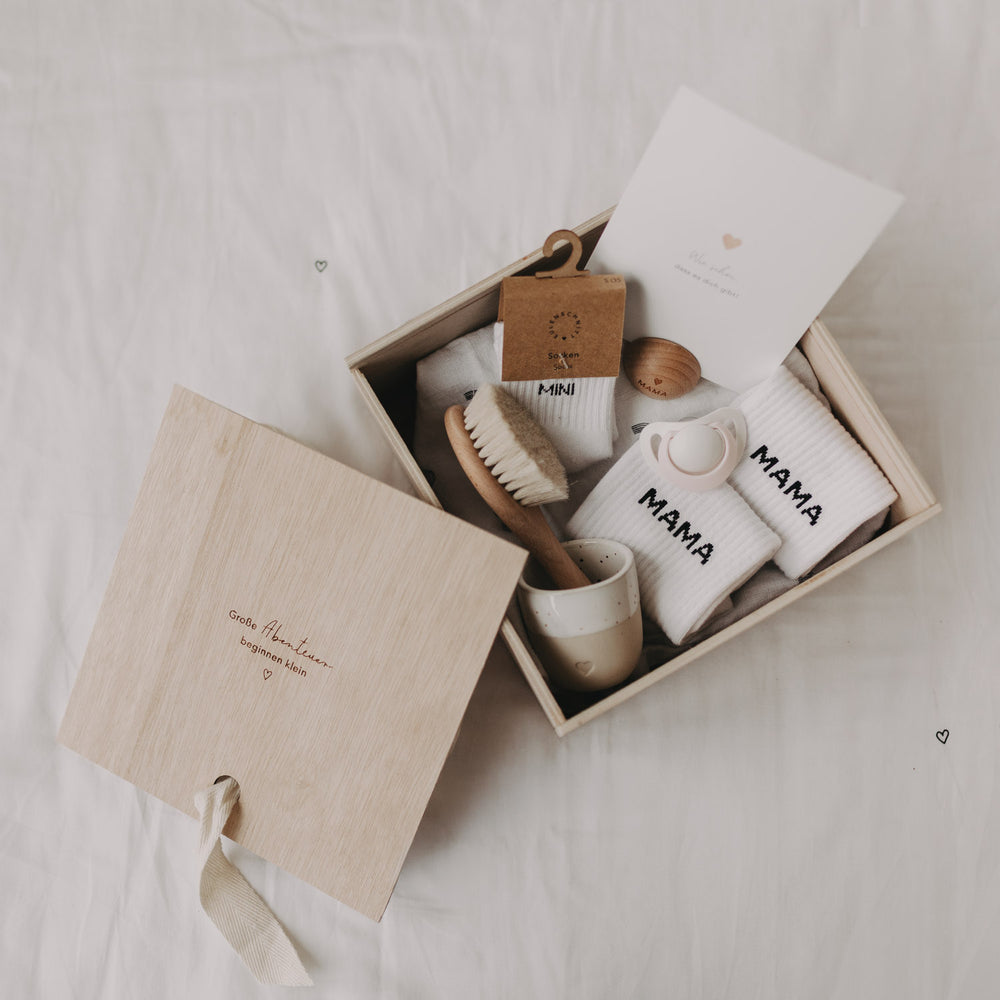 Gefüllte Erinnerungsbox mit Babyartikeln wie Socken, Bürste, Postkarte, Schnuller und Becher.