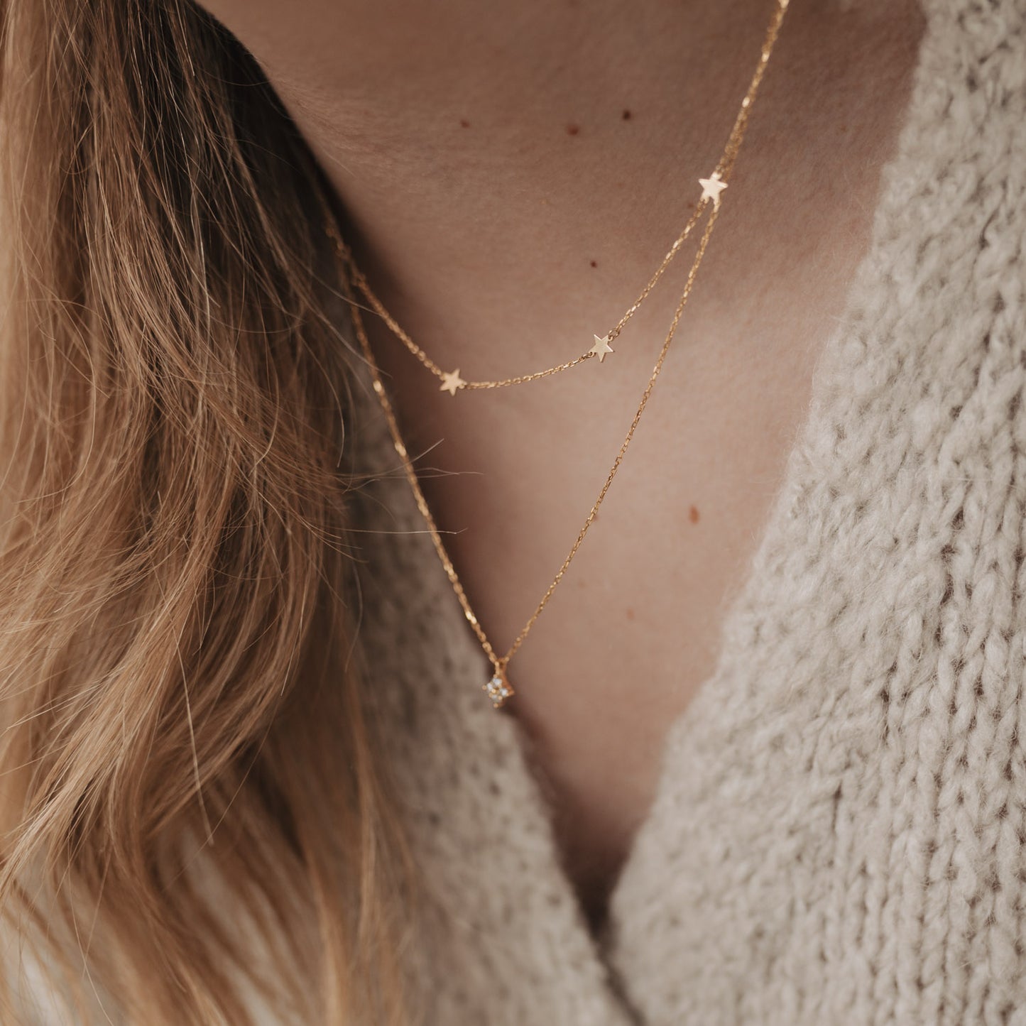 Detailansicht der Kette Jackie Gold mit kleinen Sternenanhängern, elegant getragen mit Strickpullover