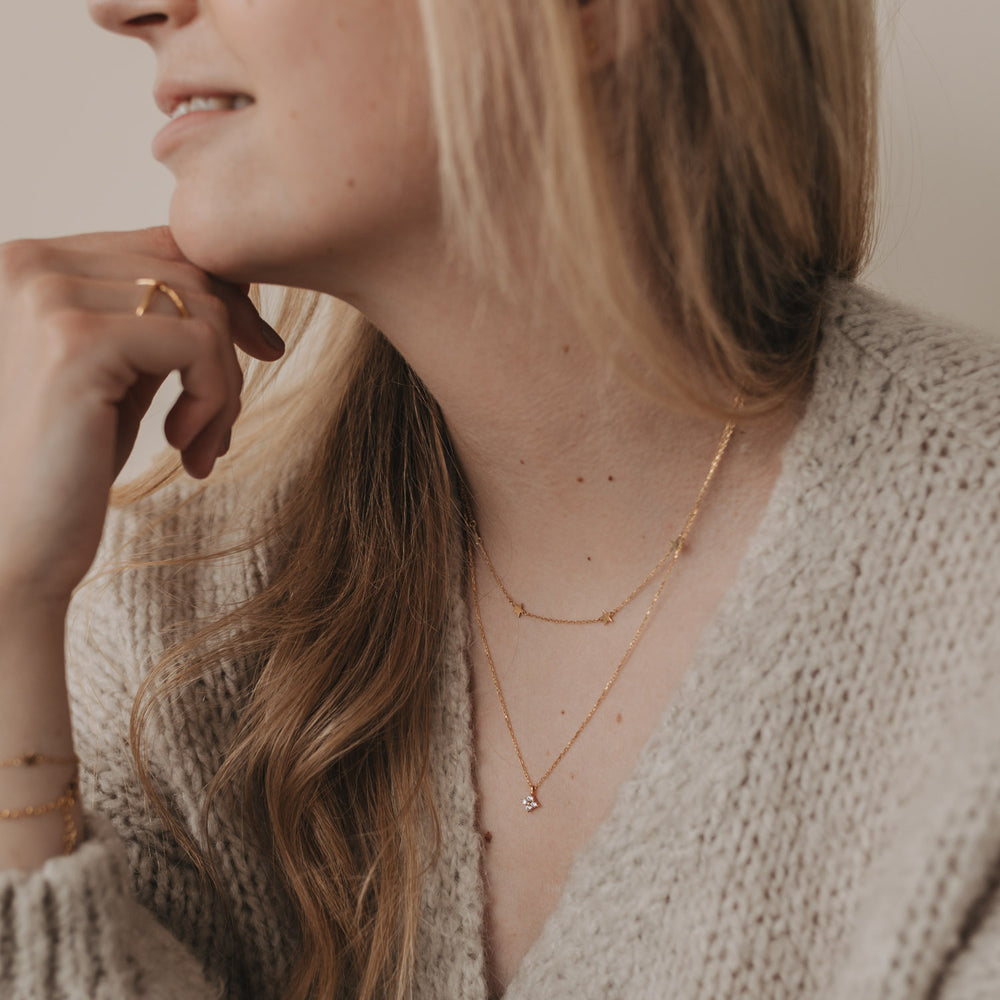 Zarte Kette Jackie in Gold mit Sternanhängern, kombiniert mit weiterer Kette, getragen am Hals einer Frau