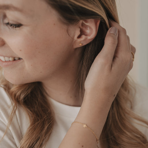 Frau trägt goldene Stern-Ohrstecker Jackie Gold und passendes Armband, eleganter Alltagslook mit feinem Schmuck.