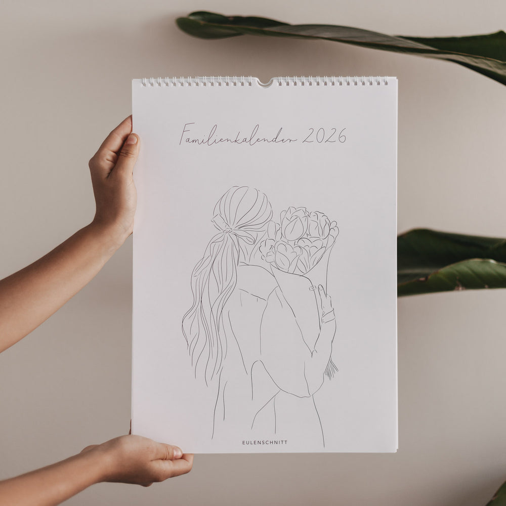 Familienkalender 2026 mit gezeichneter Frau und Blumenstrauß, hochgehalten vor beigem Hintergrund mit grünen Blättern.