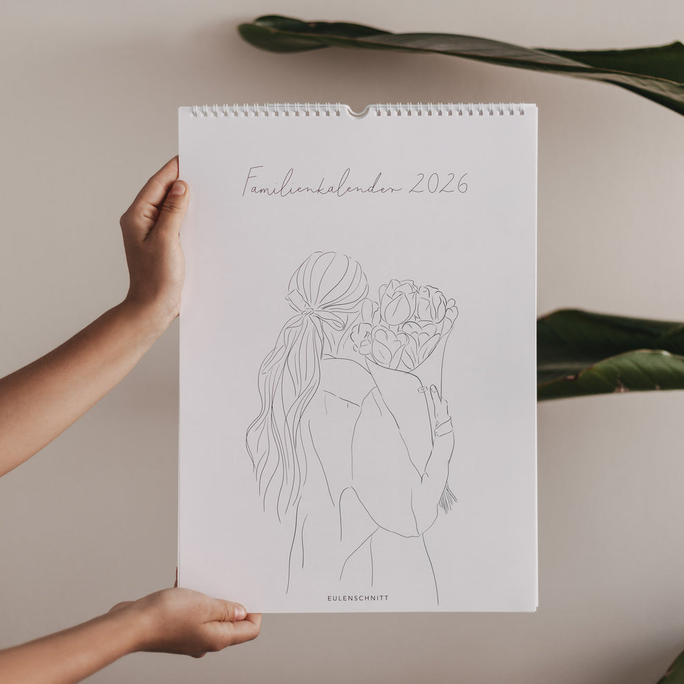 Familienkalender 2026 mit gezeichneter Frau und Blumenstrauß, hochgehalten vor beigem Hintergrund mit grünen Blättern.