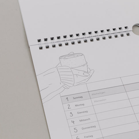 Familienkalender 2026 mit Illustration zweier Hände und Becher, Feiertage wie Allerheiligen in Spaltenübersicht sichtbar.