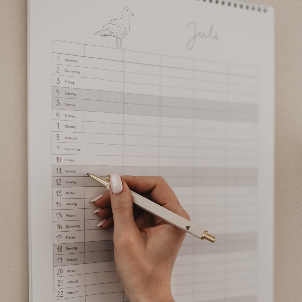 Familienkalender 2026 mit Monatsübersicht Juli, Hand trägt Eintrag mit Stift in Spaltenlayout unter Möwen-Illustration ein.
