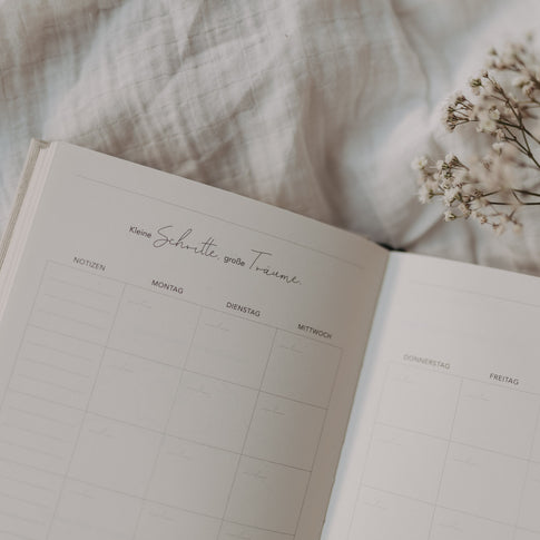 Offene Kalenderseite mit Wochenübersicht und Spruch „Kleine Schritte, große Träume“ auf weichem Stoffhintergrund.
