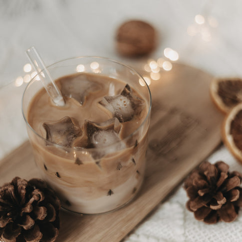 Sternförmige Eiswürfel im Glas mit Eiskaffee, arrangiert mit Winterdeko und Lichterkette.