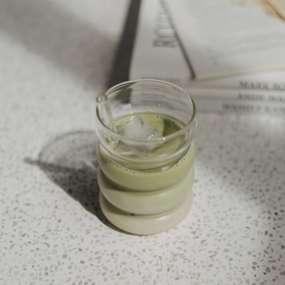 Eulenschnitt Bubble Glas mit Iced Matcha Latte, darin ein sternförmiger Eiswürfel und Strohhalm aus Glas.