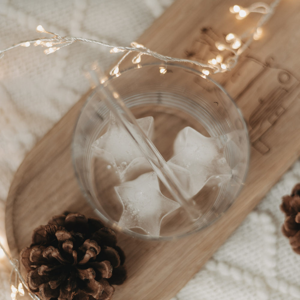 Nahaufnahme von Glas mit drei sternförmigen Eiswürfeln auf einem Tablett mit Zapfen und Licht.