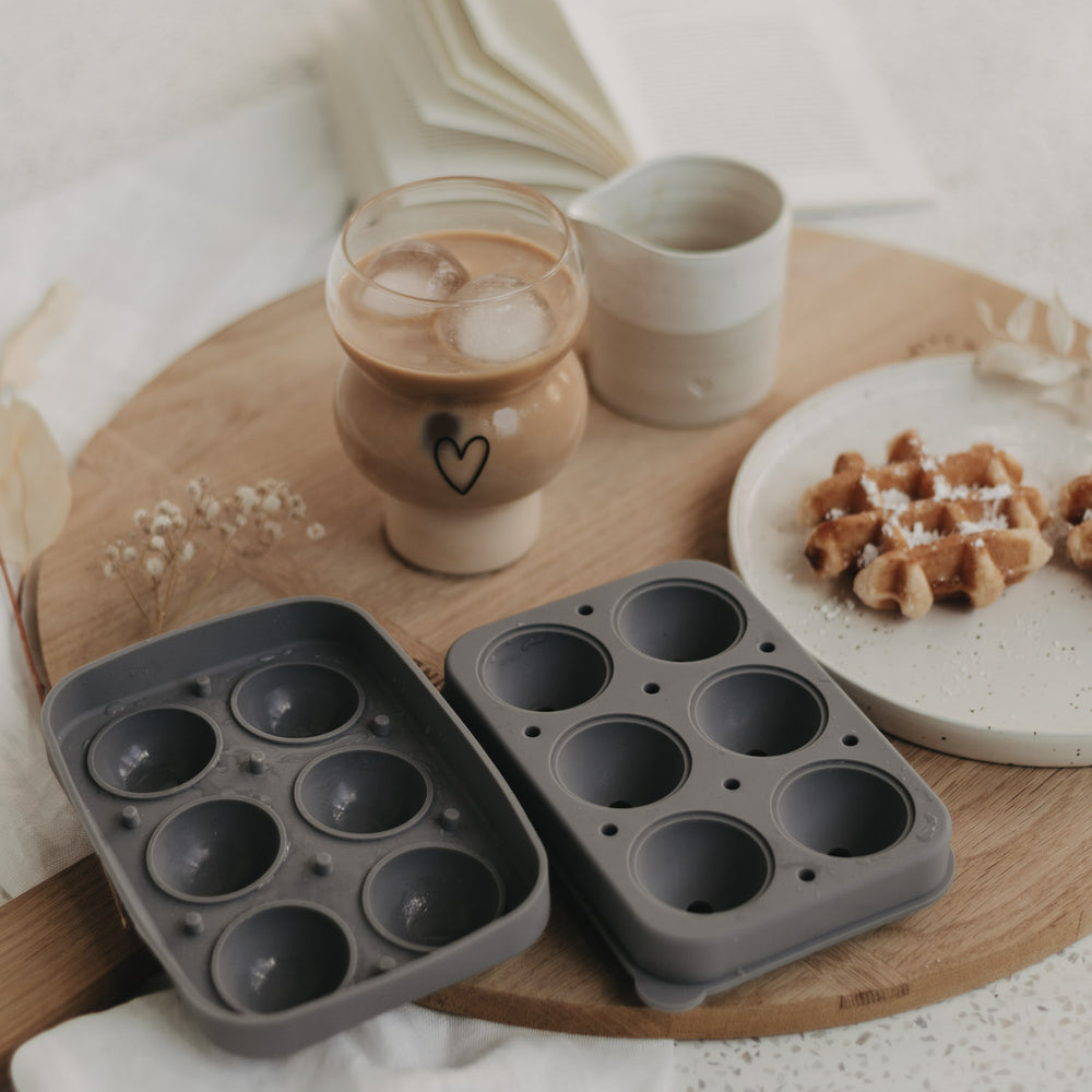 Szenenbild mit geöffneter Form, Glas mit Eis-Kugeln und Waffeln auf Holzbrett.