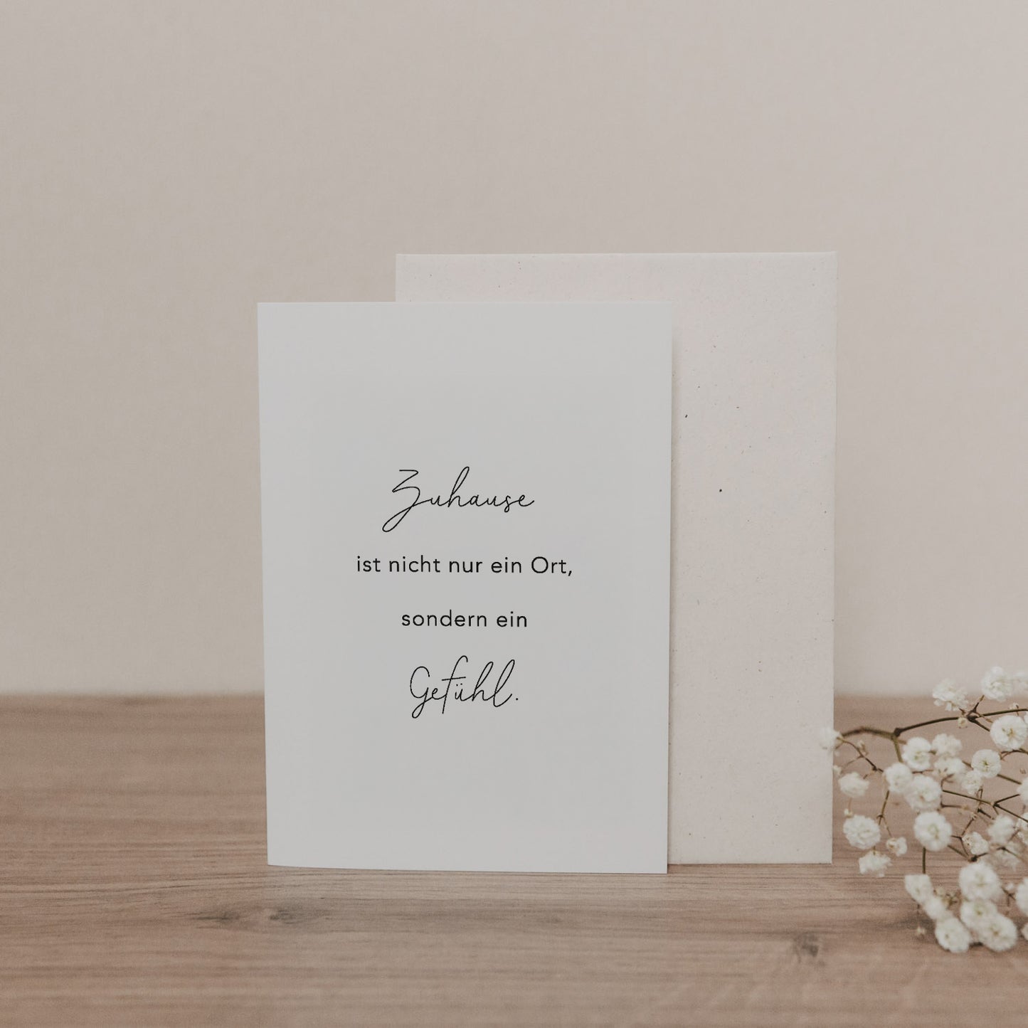 Klappkarte mit dem Spruch „Zuhause ist nicht nur ein Ort, sondern ein Gefühl“ und passendem Umschlag, dekorativ arrangiert.