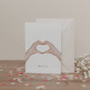 Klappkarte mit zwei Händen in Herzform und dem Schriftzug „Alles Liebe“, vor Umschlag und Blumen, auf hellem Untergrund.