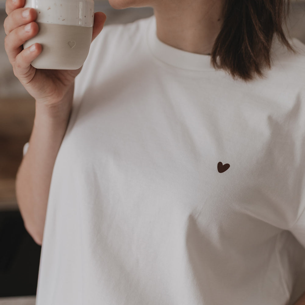 Frau trinkt Kaffee, Nahaufnahme des kleinen Herzprints auf der Brust des weißen T-Shirts.