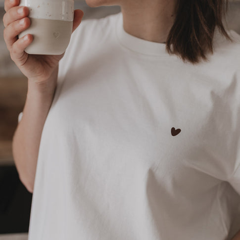 Frau trinkt Kaffee, Nahaufnahme des kleinen Herzprints auf der Brust des weißen T-Shirts.