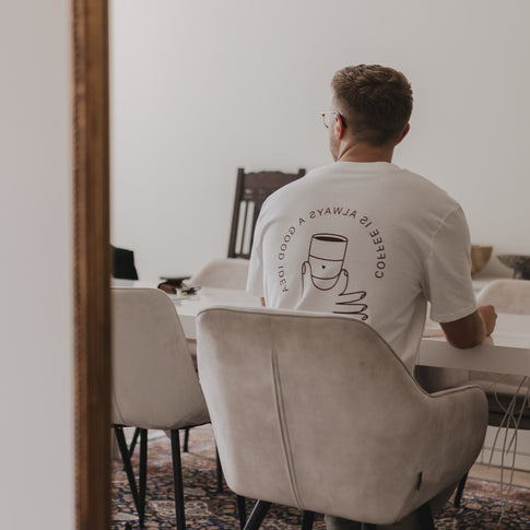 Mann sitzt am Esstisch im Coffee T-Shirt mit Rückseitendruck einer Hand mit Kaffeetasse und Slogan