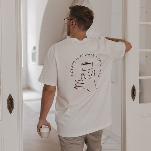 Rückansicht eines Mannes mit Coffee T-Shirt beim Kaffeetrinken in heller Küche mit Glastür