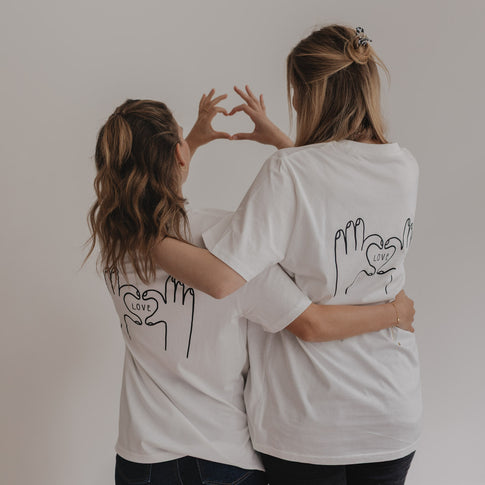 Zwei Frauen zeigen gemeinsam mit den Händen ein Herz über dem LOVE-Print