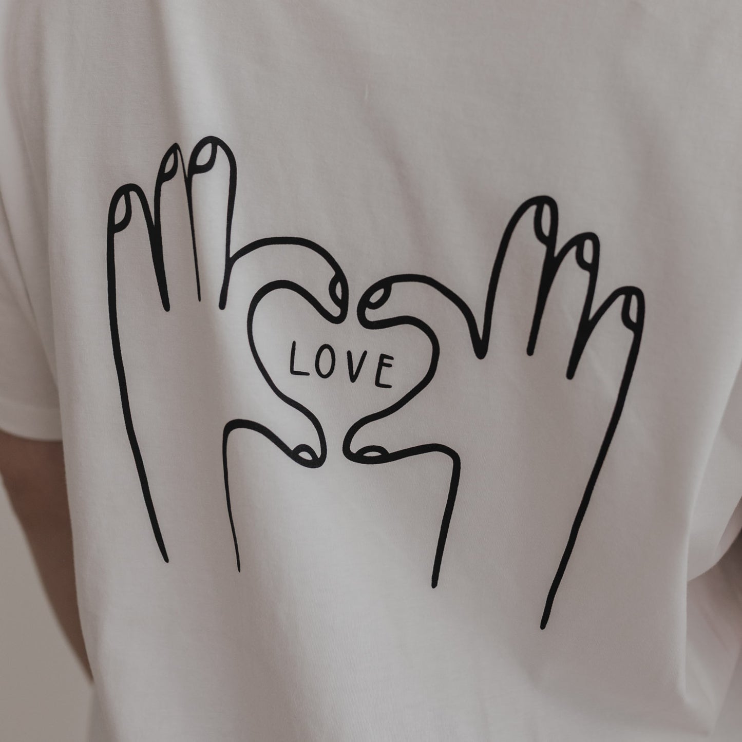 Close-up Rückenansicht LOVE Shirt mit schwarzem Herz-Hand-Motiv auf Weiß