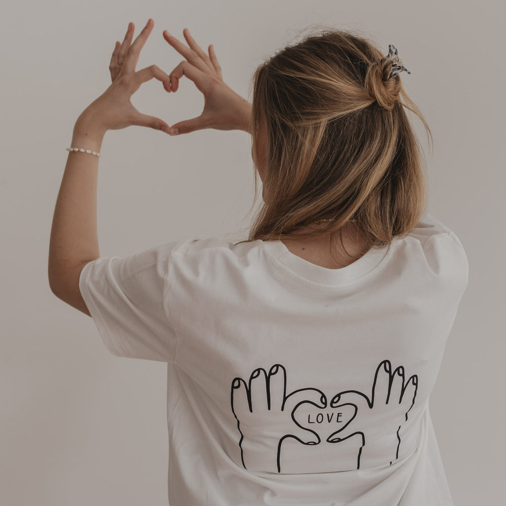 Frau formt mit Händen ein Herz, passend zum T-Shirt-Motiv auf dem Rücken
