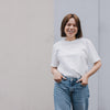 Frau im weißen T-Shirt mit kleinem Herzprint, lässiger Look vor neutralem Hintergrund