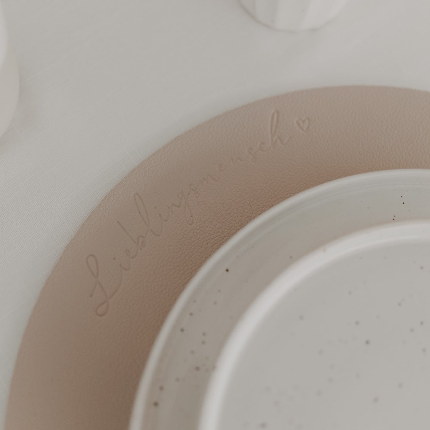 Platzset in Beige-Creme mit eingeprägtem Schriftzug „Lieblingsmensch“ unter Keramikteller.