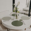 Rund gedeckter Tisch mit grünen wendbaren Platzsets und Blumendekoration.